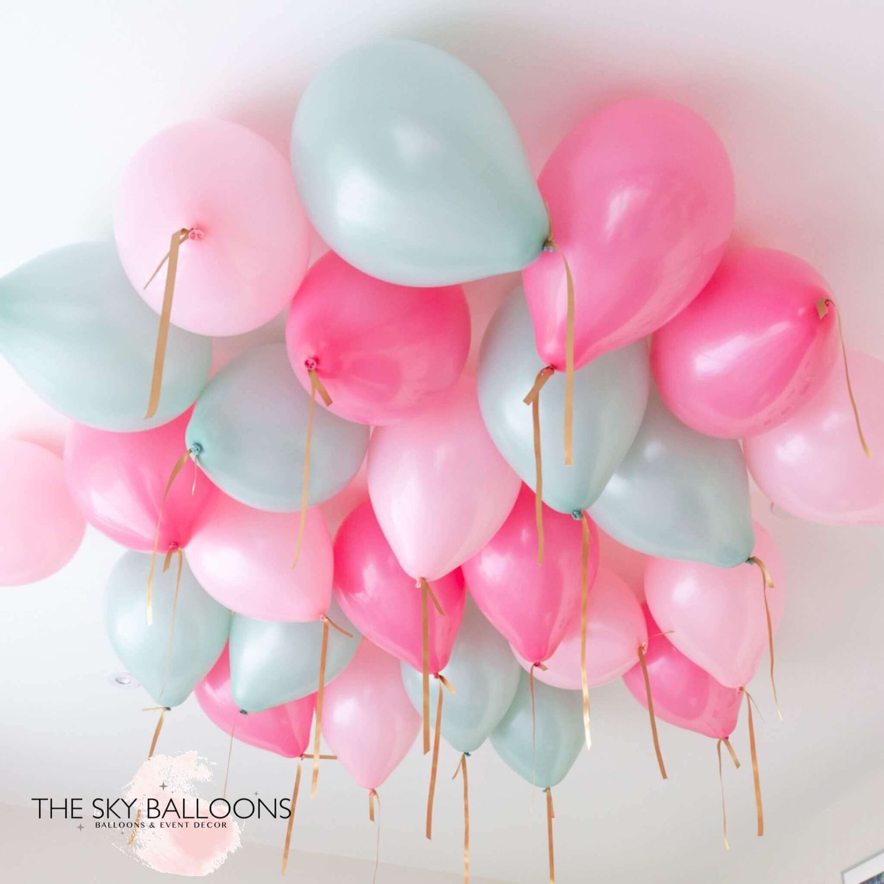 A cluster of round helium balloons in shades of pink and mint green, attached to strings, meant for ceiling decoration.