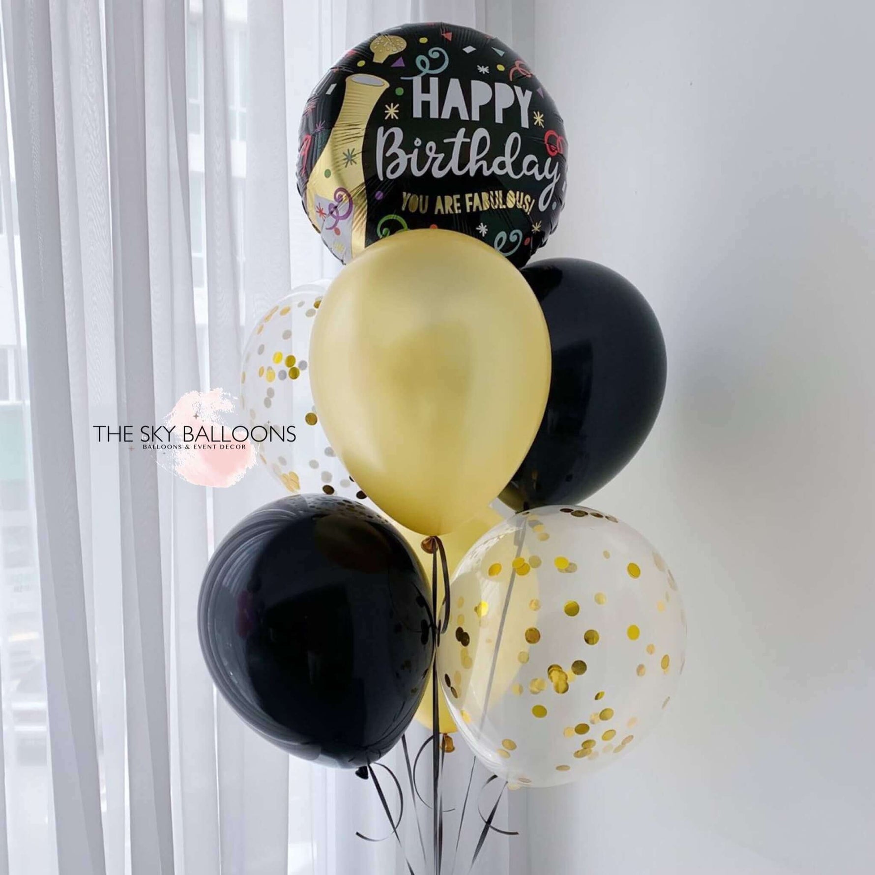 A bouquet of helium-filled birthday balloons in gold, black, and white colors with 'Happy Birthday' and other birthday-related messages printed on them.