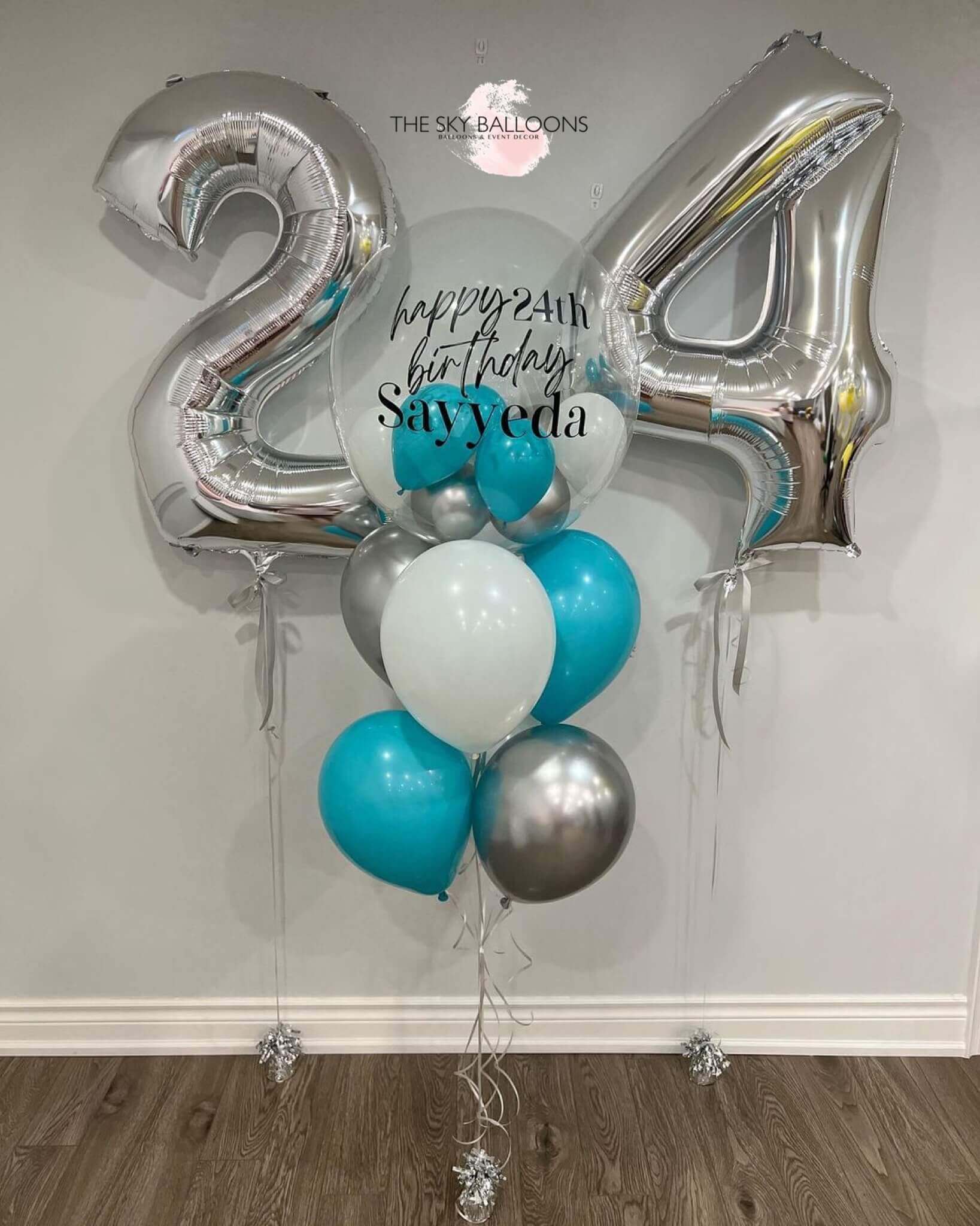 A numerical balloon bouquet with the numbers '24' in silver, surrounded by blue and silver balloons, with helium gas, including customized text 'Happy Birthday' and a name 'Sayed'.
