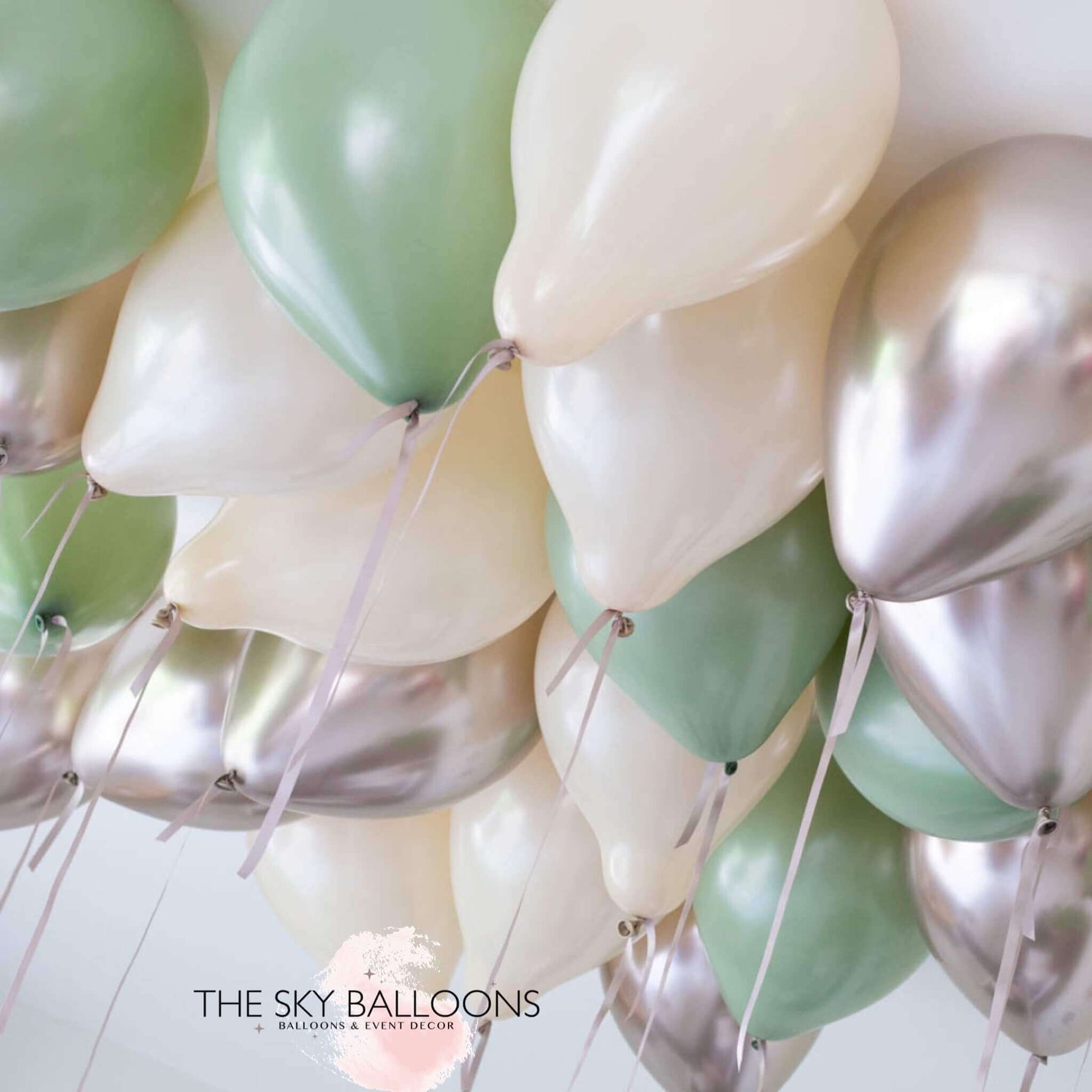 A cluster of inflated balloons in shades of green, white, and silver, attached to strings, presumably intended for ceiling decoration.