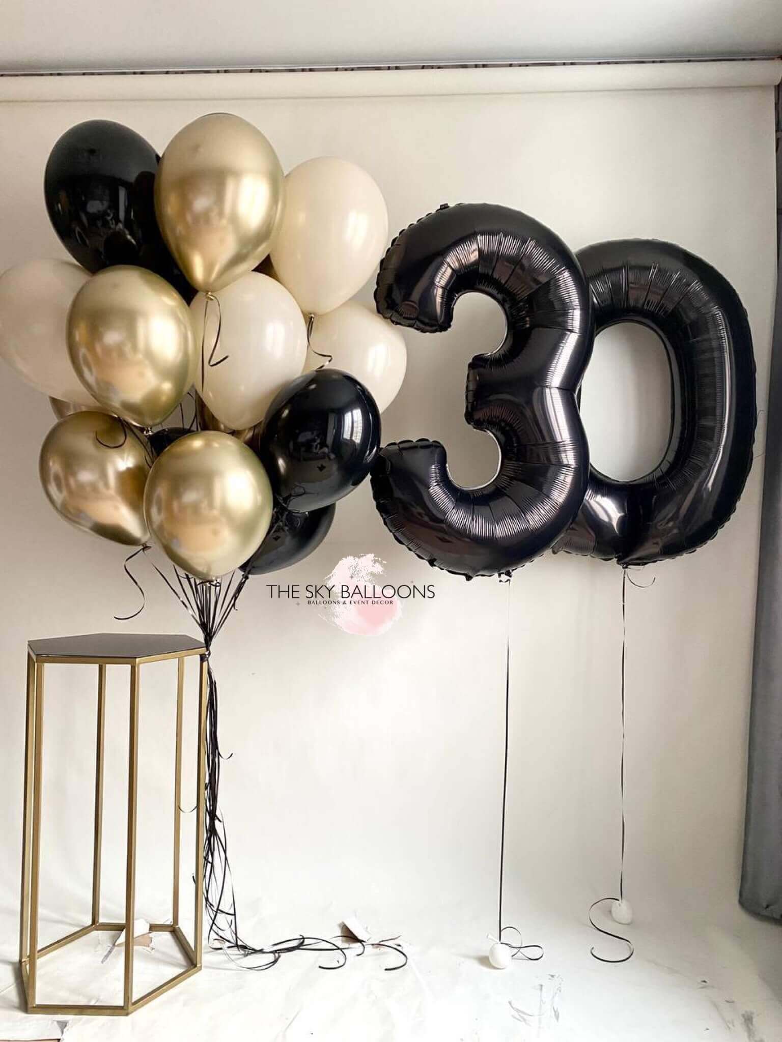 A bouquet of balloons featuring gold, black, and white colors, with large black numerical foil balloons '30' included.