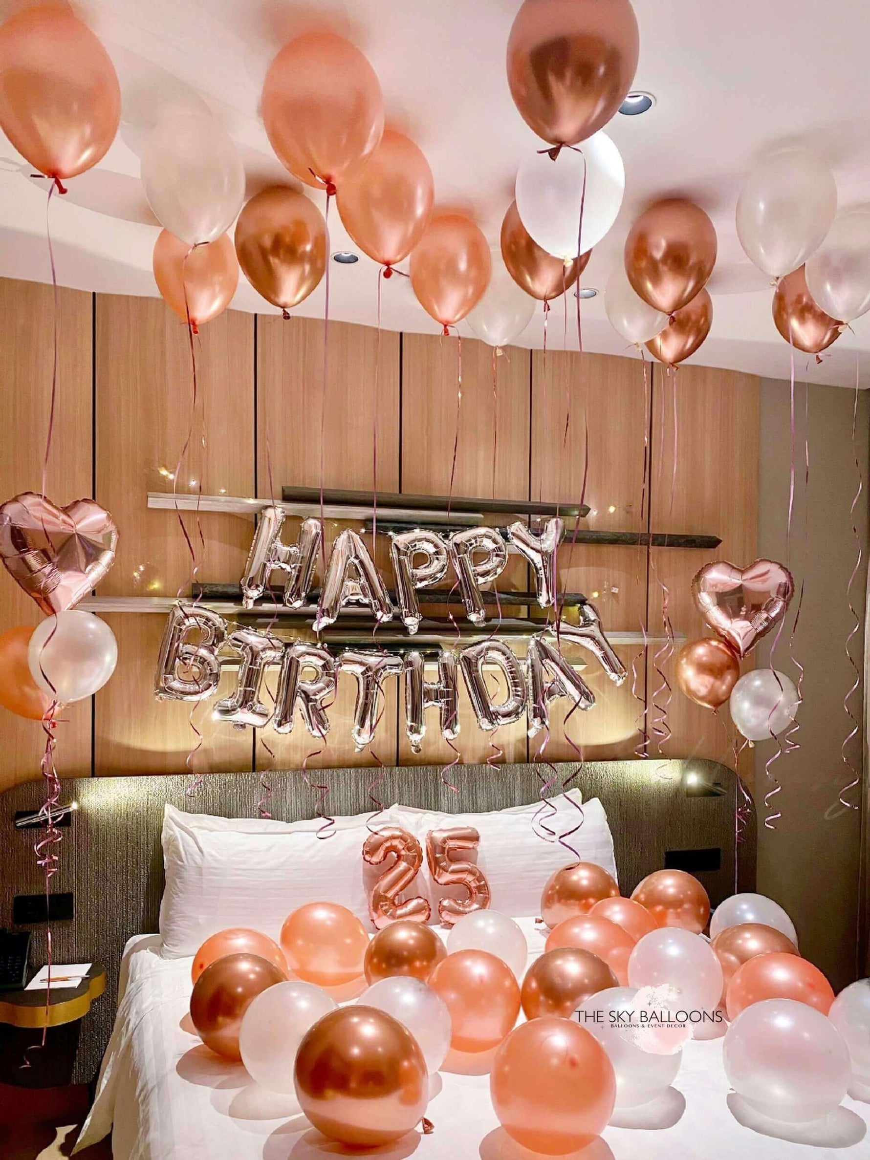 A room decorated with a 'Happy Birthday' banner, balloons in shades of pink and gold, and number foils.