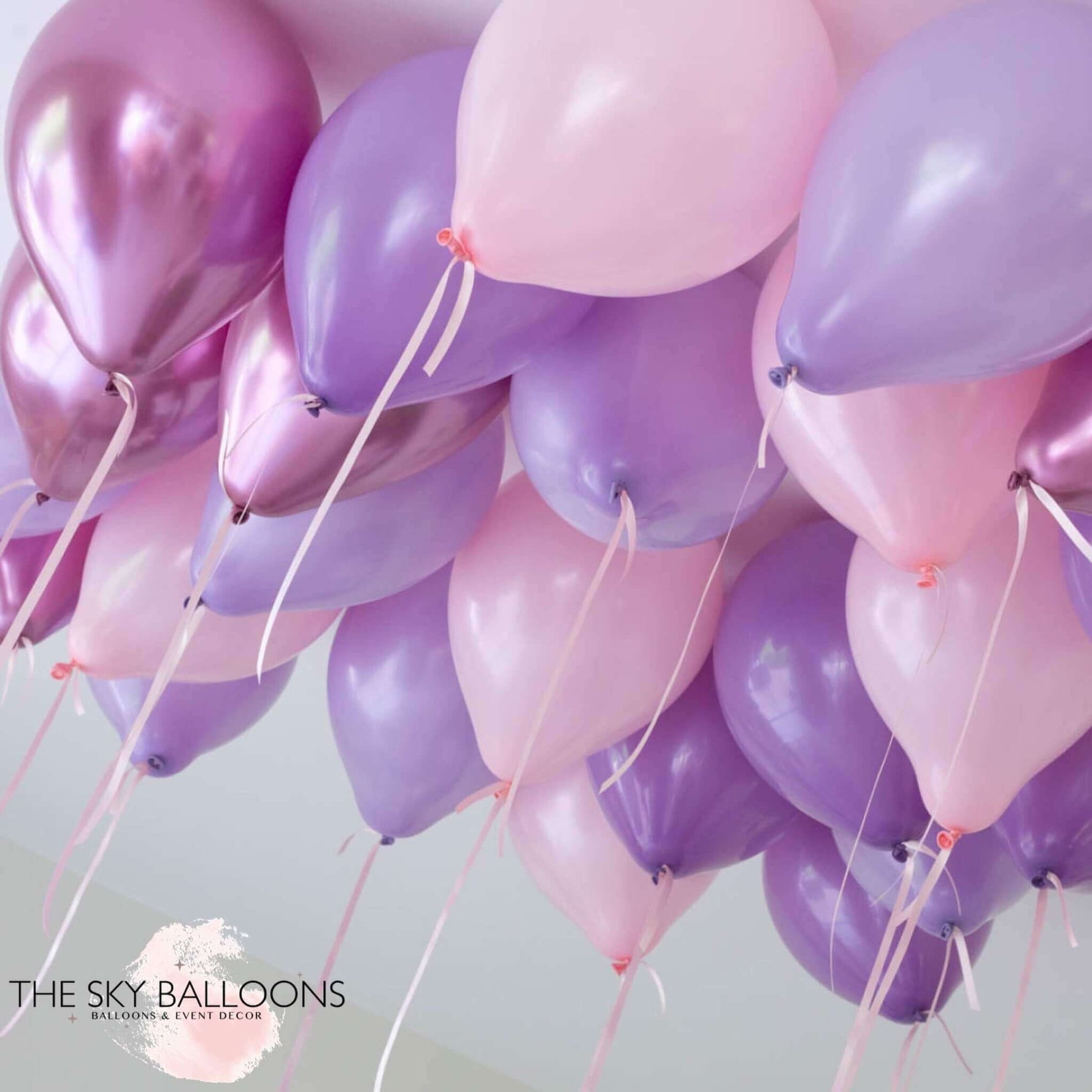 A cluster of inflated balloons in shades of purple, pink, and lavender, attached to strings, intended for ceiling decoration.