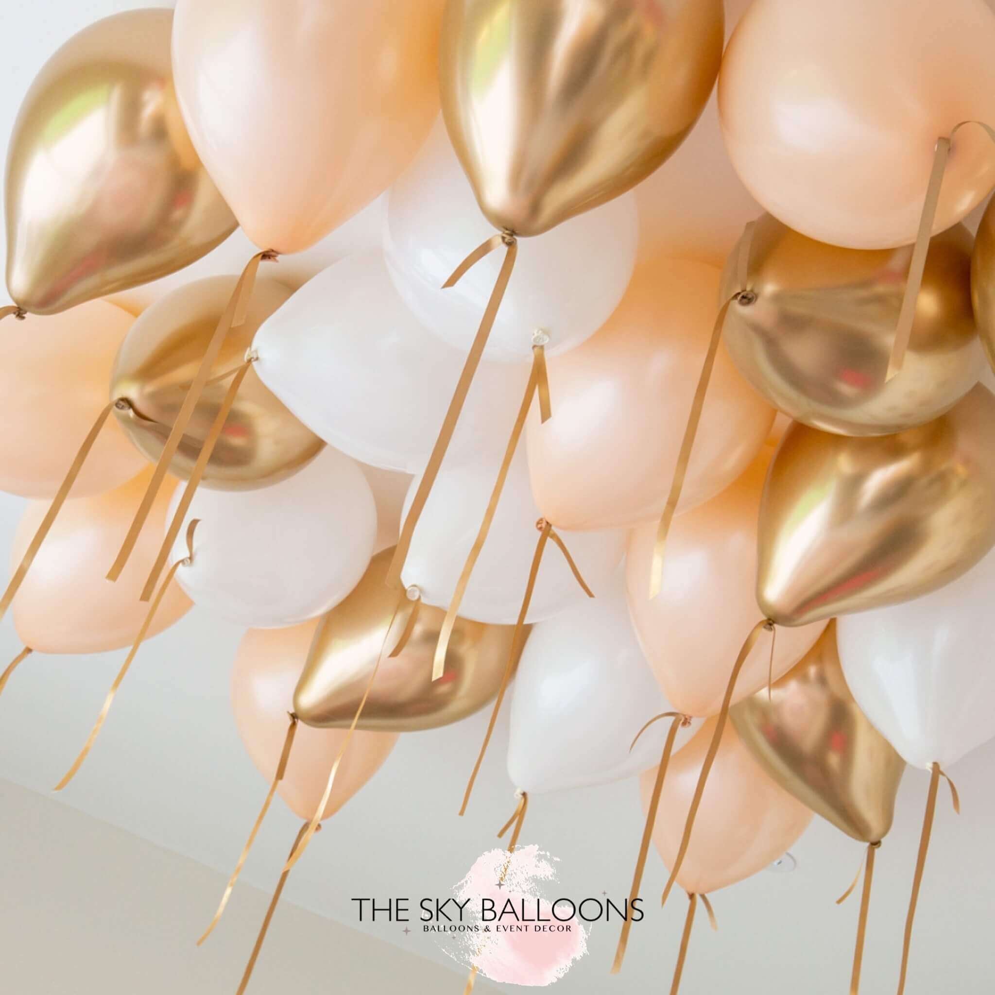 A cluster of helium-filled ceiling balloons in peach and chrome colors, attached to strings, ready to float.