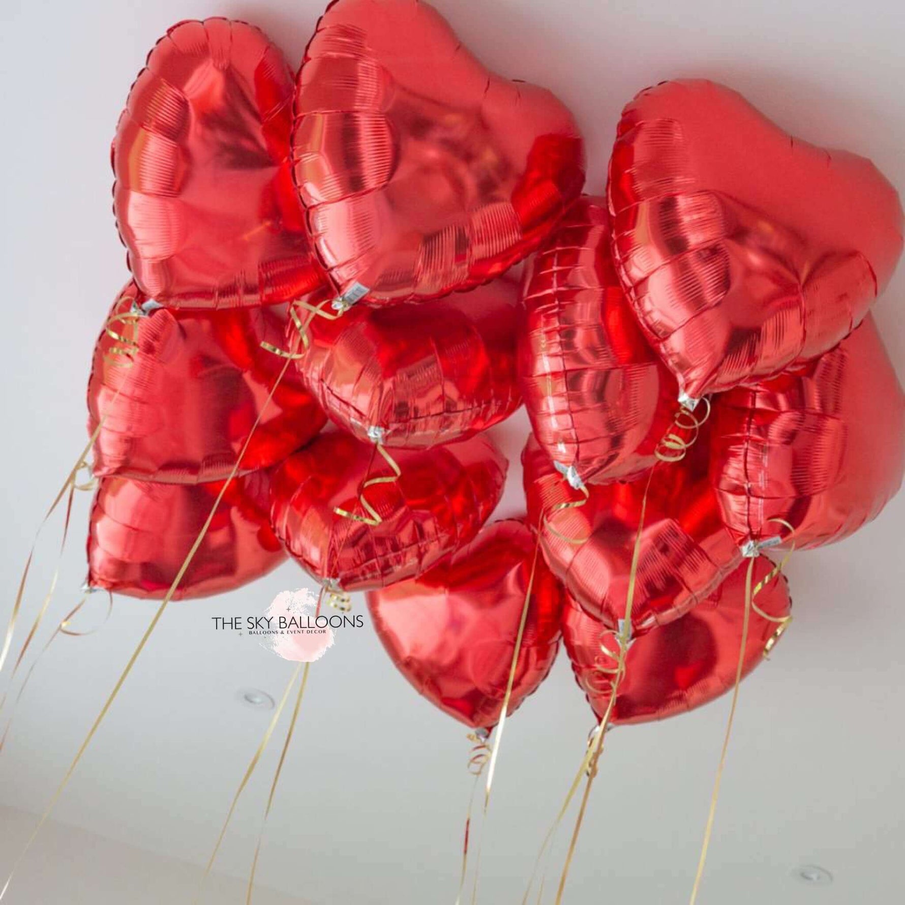 A bunch of red heart-shaped balloons attached to strings, displayed against a neutral background.