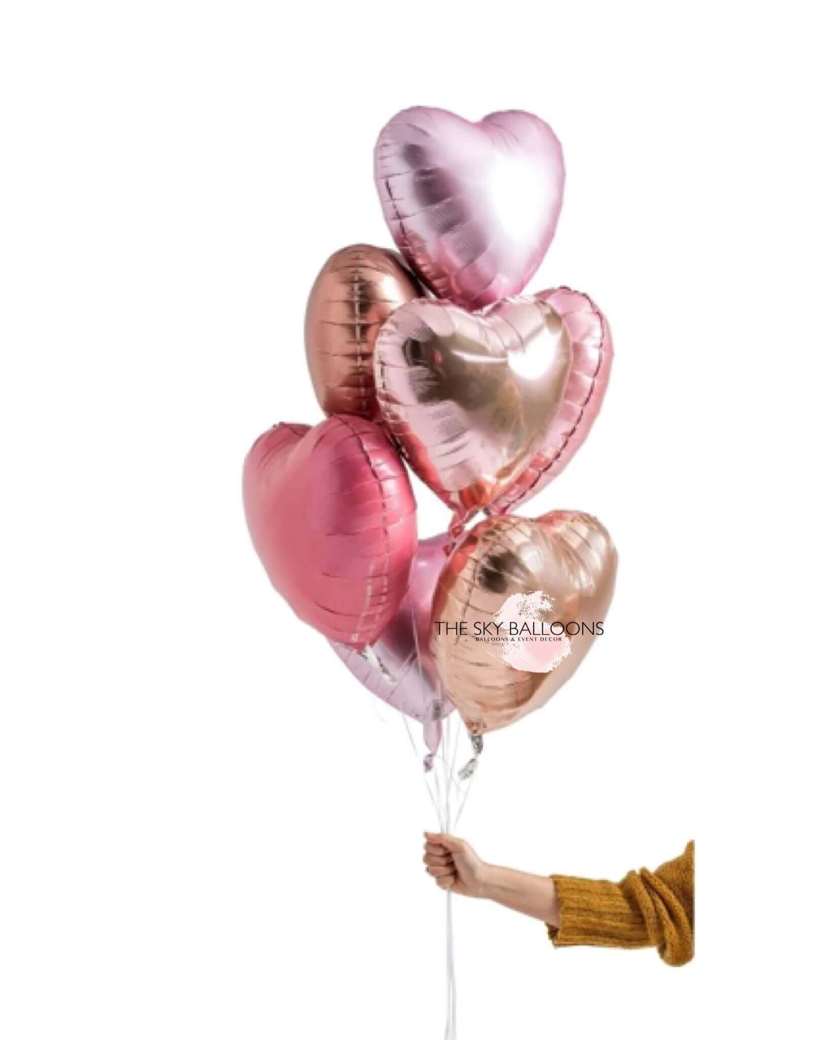 A hand holding a bouquet of rose gold balloons with heart and star shapes, weighted down with helium.
