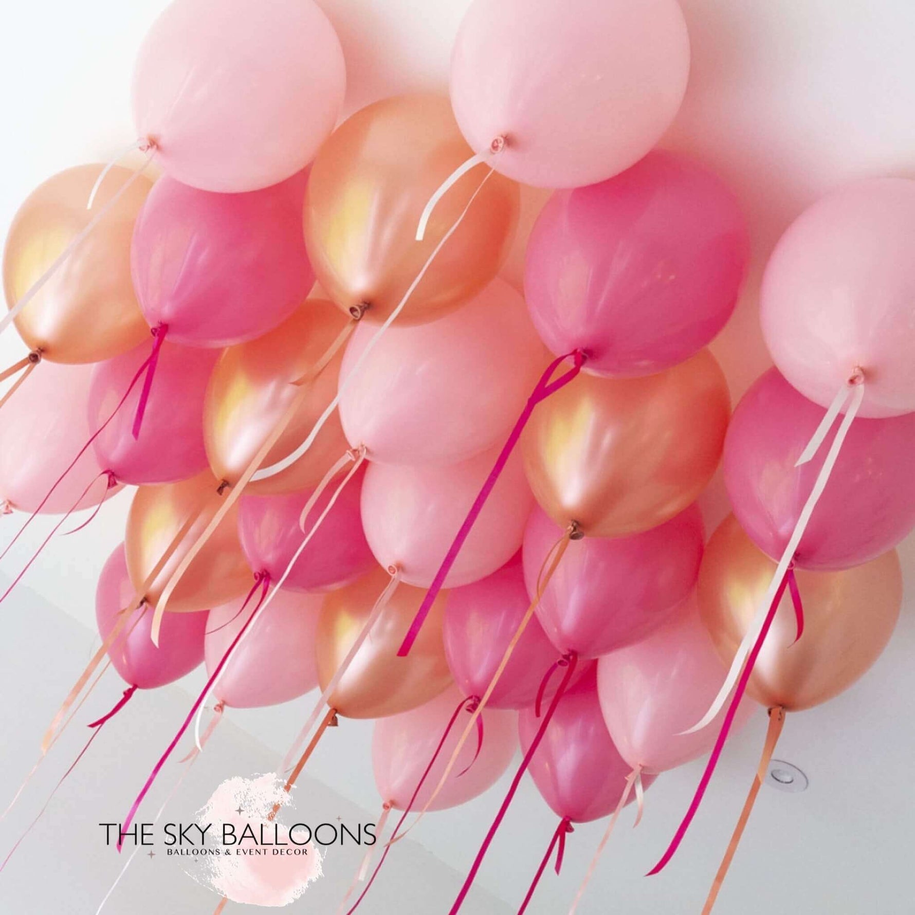 A cluster of rose pink and gold helium ceiling balloons attached to strings, displayed against a white background.
